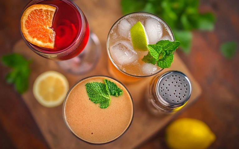 Una selezione di mocktail e cocktail no-low alcolici serviti in bicchieri decorati, con dettagli di fiori ed erbe aromatiche su una tavola in legn